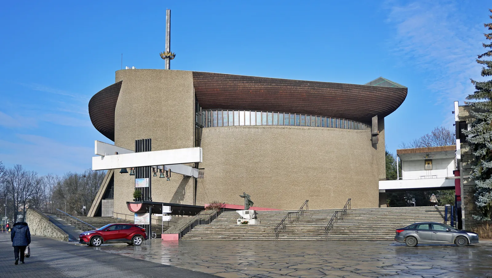 The Lord's Ark church in Nowa Huta, a windowless hull-shaped building of pebble-faced concrete under a sweeping copper roof, with a tall metal mast rising from its prow and steps up to the entrance