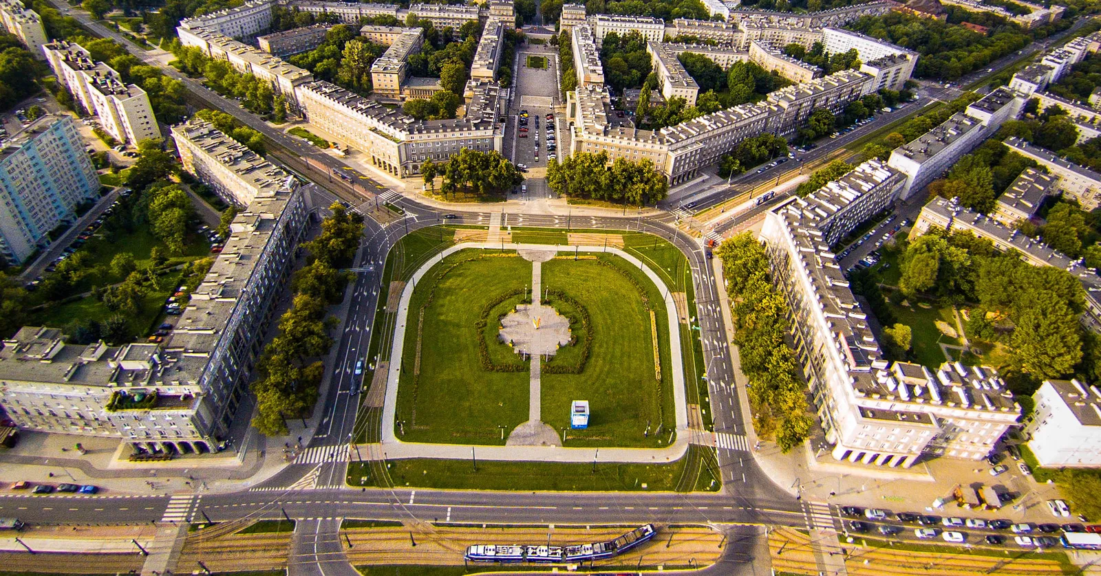 Plac Centralny in Nowa Huta seen from directly above, a rectangle of lawn ringed by roads with arcaded five-storey blocks around it and wide tree-lined avenues running away from its corners