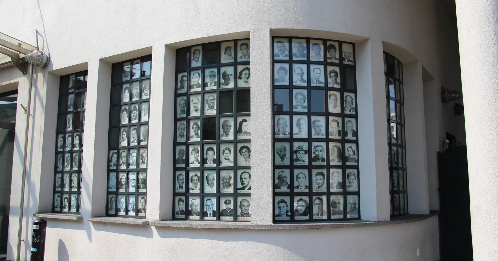 The white curved entrance front of Oskar Schindler's former enamel factory in Kraków, its tall grid windows filled with hundreds of small black and white portrait photographs of survivors