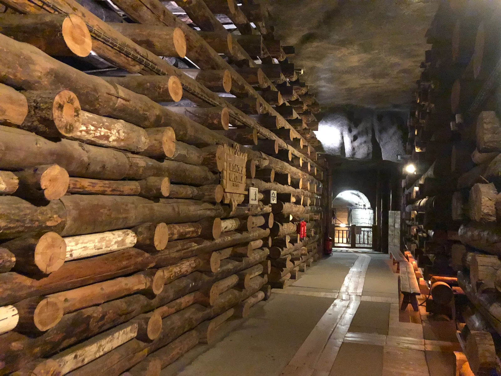 A gallery in the Wieliczka salt mine walled and roofed with stacked pine logs, cut ends facing the passage, a lit corridor running away into the rock at the far end