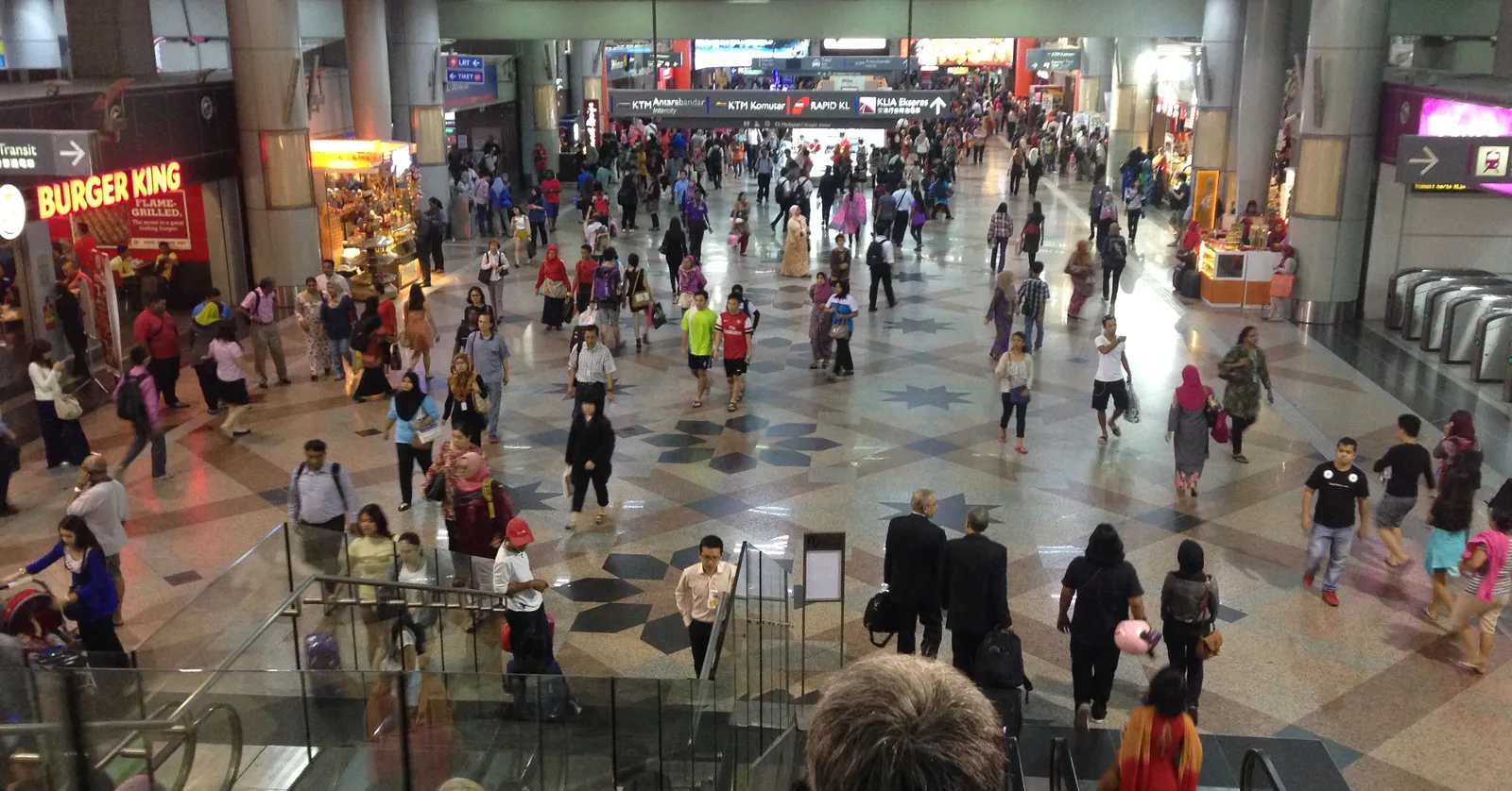 The main concourse of KL Sentral station in Kuala Lumpur seen from above, a patterned stone floor crowded with travellers and shopfronts along both sides