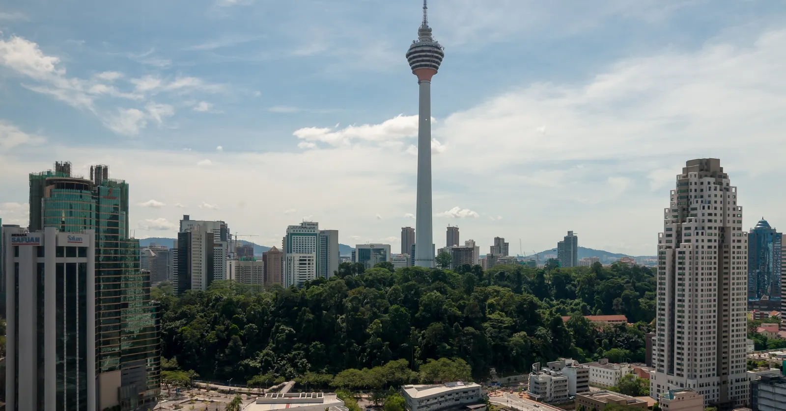 Menara Kuala Lumpur rising above the city, its ringed head and antenna mast standing clear of the surrounding office towers with the green hill of Bukit Nanas at its base