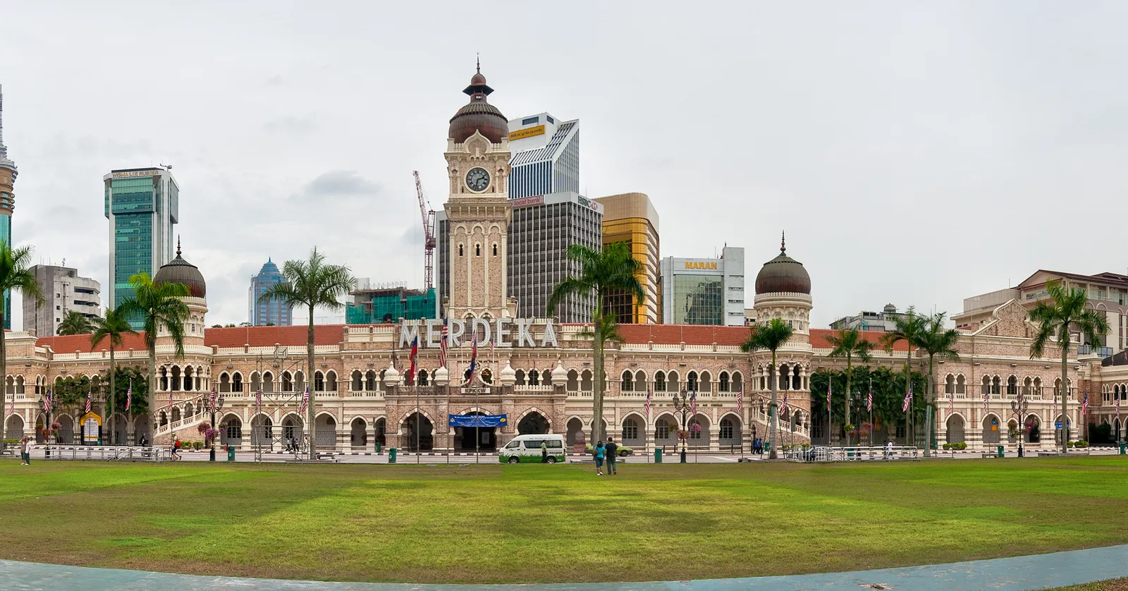 Merdeka Square in Kuala Lumpur, the flat green field in the foreground and the long arcaded frontage and copper-domed clock tower of the Sultan Abdul Samad Building running along the far side