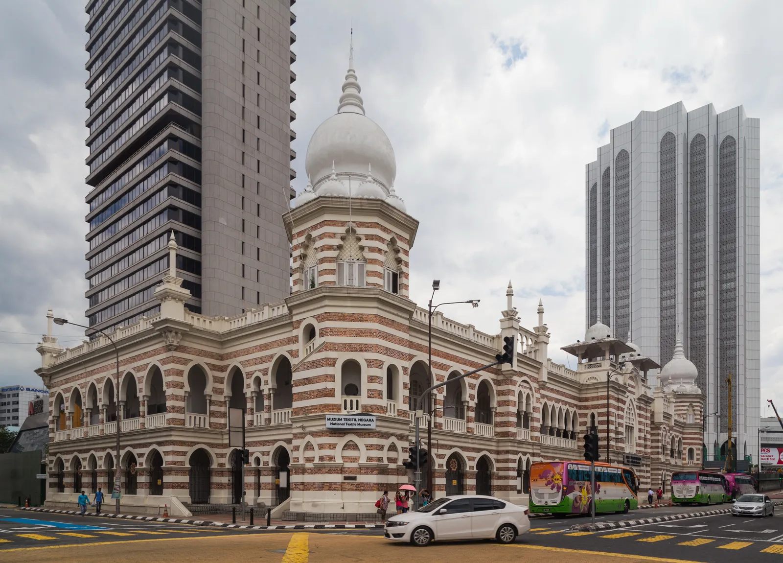 The National Textile Museum in Kuala Lumpur on its street corner, a pink and white banded brick building with horseshoe arches and a white onion dome, modern office towers behind it