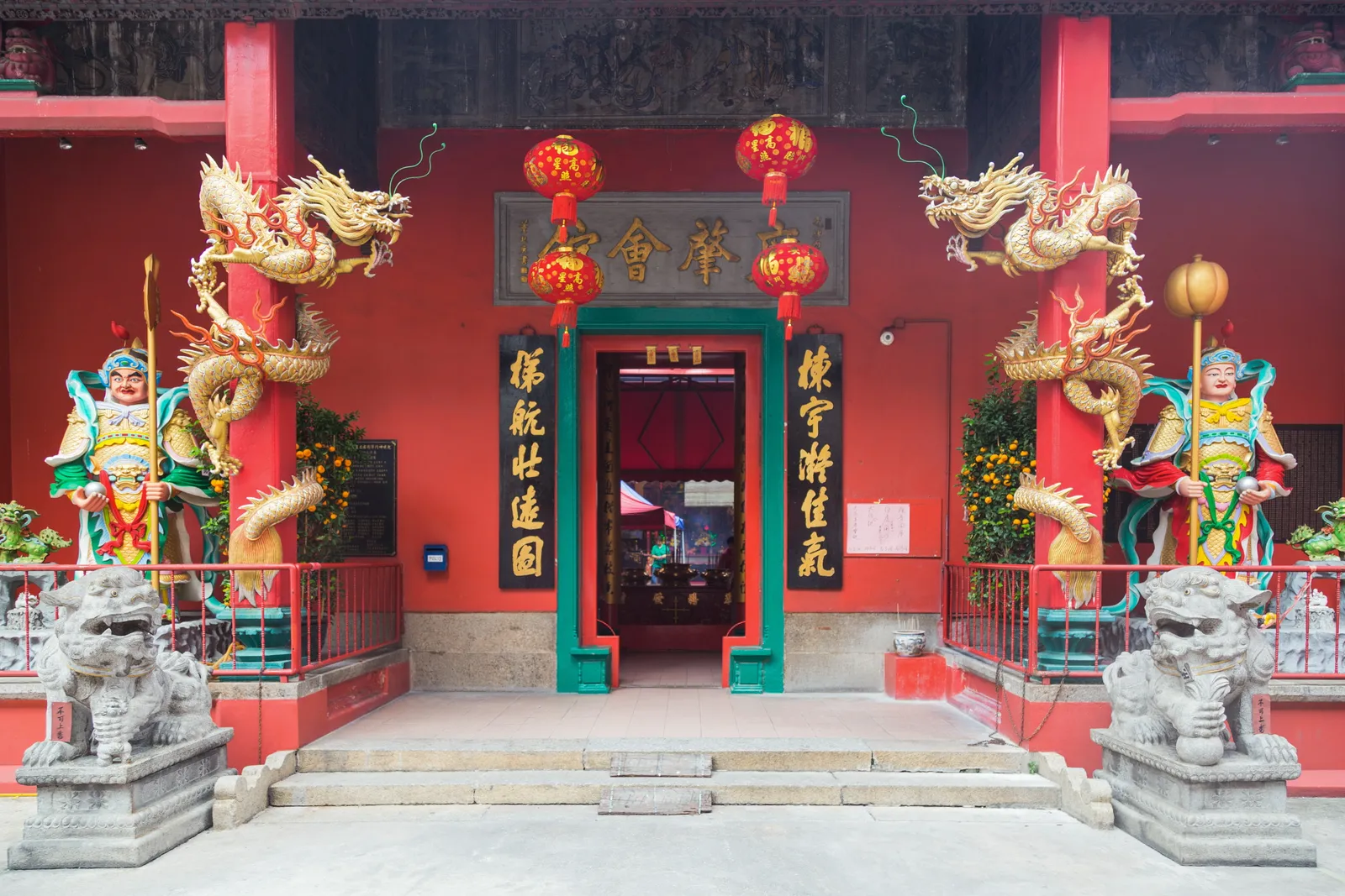 The red frontage of Guan Di Temple on Jalan Tun H S Lee in Kuala Lumpur, gold dragons coiled up the columns either side of the doorway and painted guardian figures and stone lions on the step
