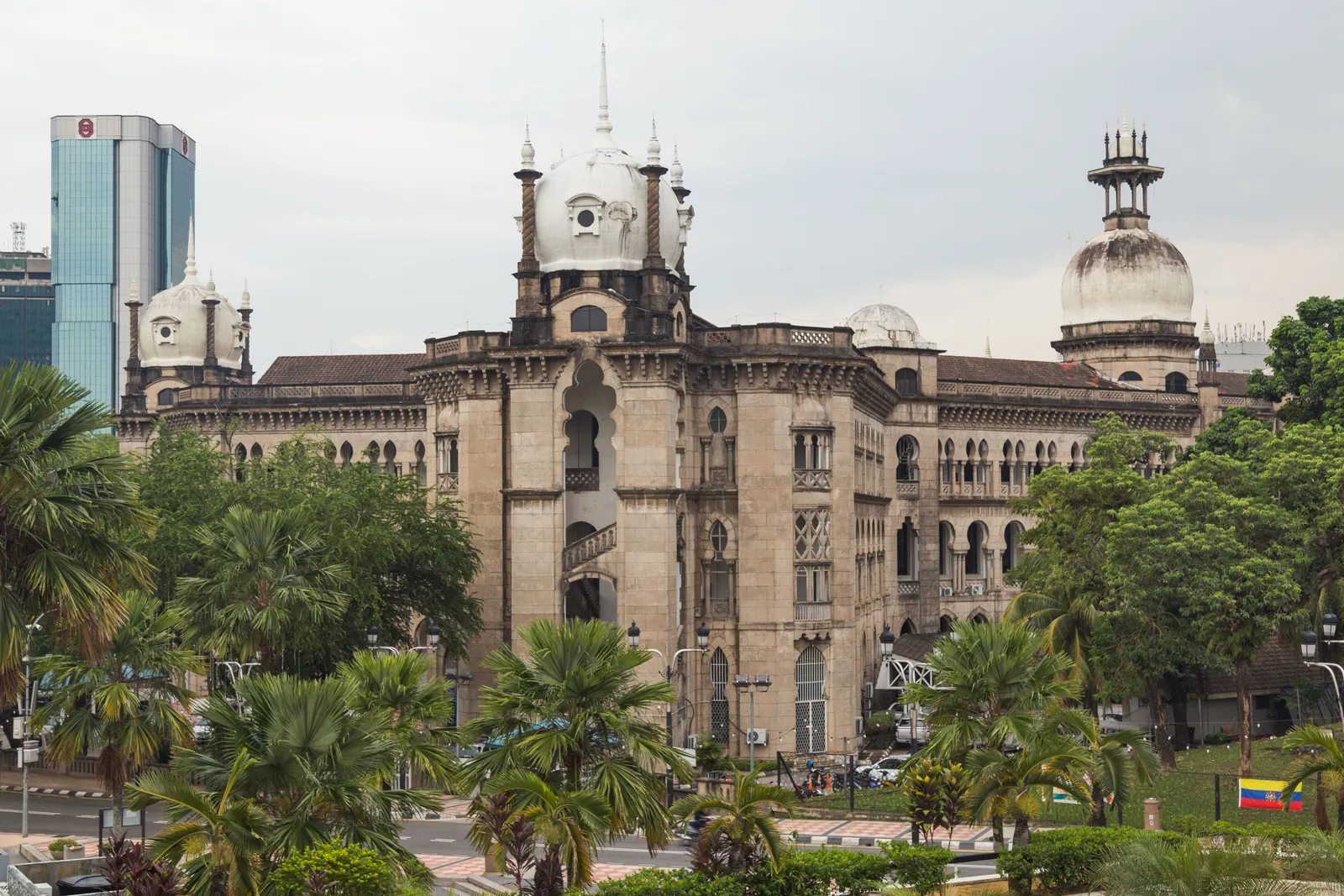 The Railway Administration Building in Kuala Lumpur behind palm trees, a heavy stone block with arcaded upper floors, corner turrets and a domed central tower