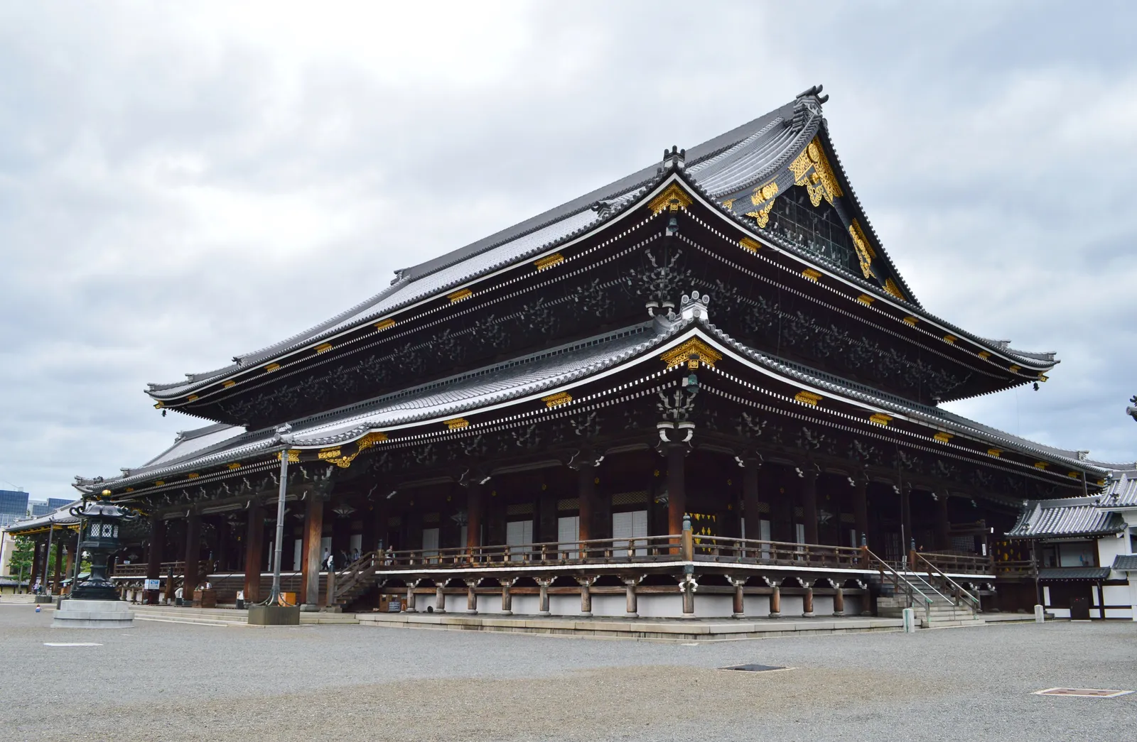 The Goeido hall at Higashi Honganji in Kyoto, an enormous dark wooden temple building on a raised stone platform with a deep tiled roof and gilded carving under the gable