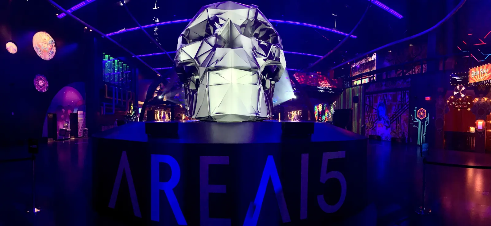 The lobby of Area15 in Las Vegas, lit purple and blue, with AREA15 in large letters across a plinth and a faceted metallic sculpture standing behind it