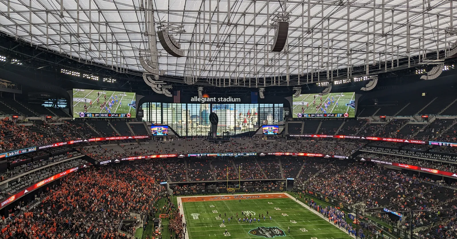 The inside of Allegiant Stadium during a football game, the white cable-hung roof structure overhead, video boards reading allegiant stadium above the far end and a full bowl of spectators around the green field
