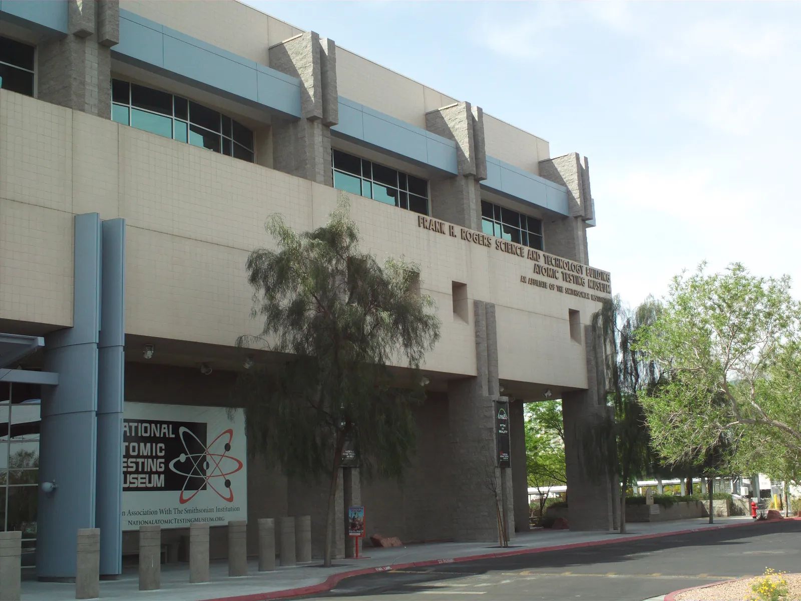 The low concrete and blue-panelled building housing the National Atomic Testing Museum in Las Vegas, with the museum's atom-symbol banner hung by the entrance