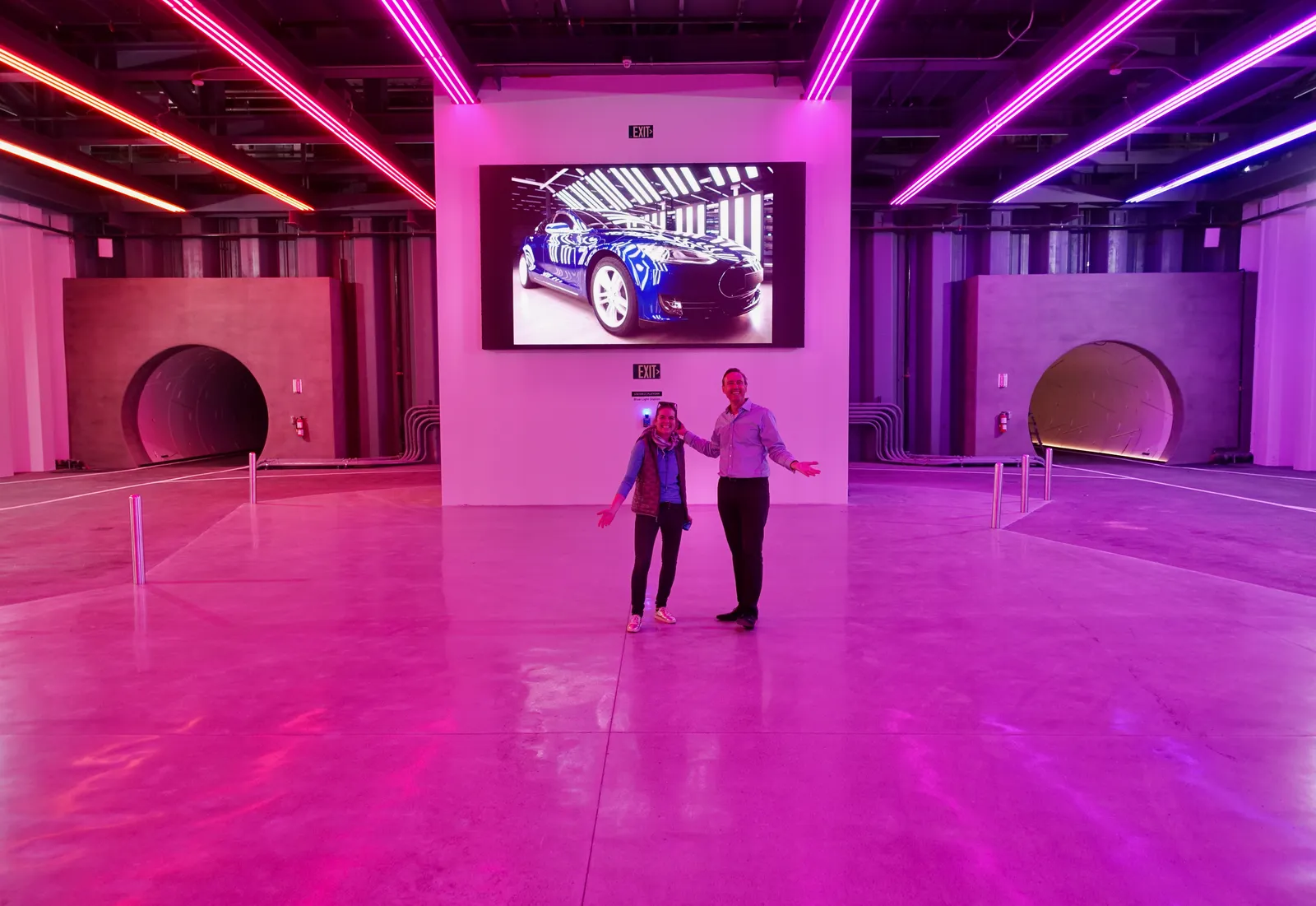 An underground station on the Las Vegas Convention Center Loop, a wide pink-lit concrete hall with two round tunnel mouths on either side of a video screen
