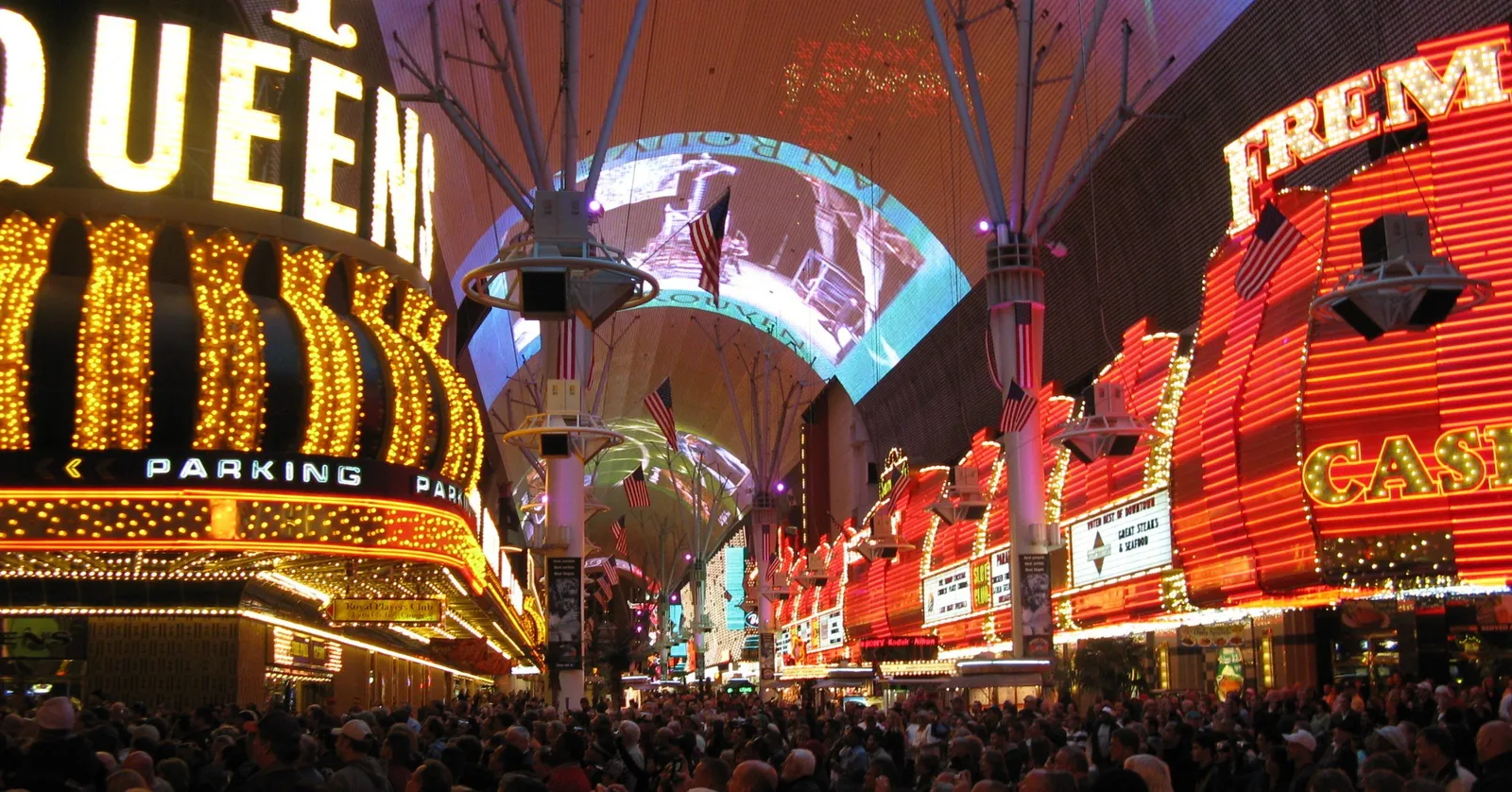 The Fremont Street Experience canopy lit overhead with the Four Queens and Fremont Hotel neon signs on either side and a dense crowd filling the pedestrian mall below