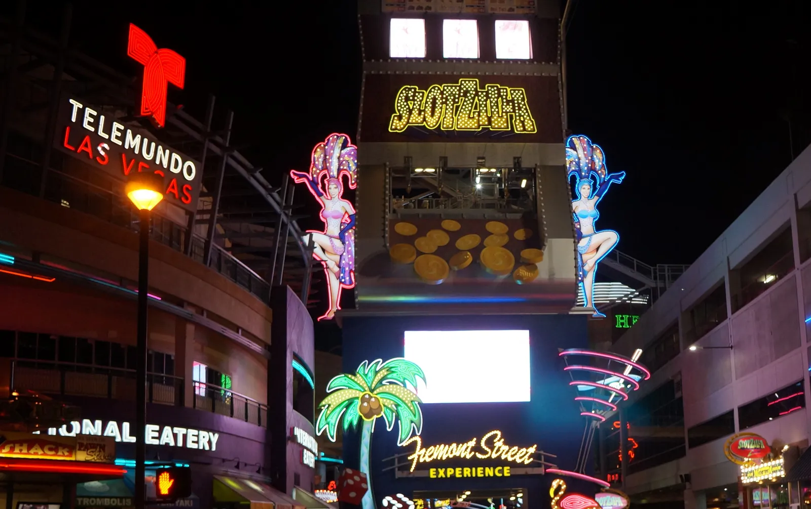The SlotZilla launch tower over Fremont Street at night, built as a giant slot machine with lit reels and neon showgirl figures either side of it, with the Fremont Street Experience sign below