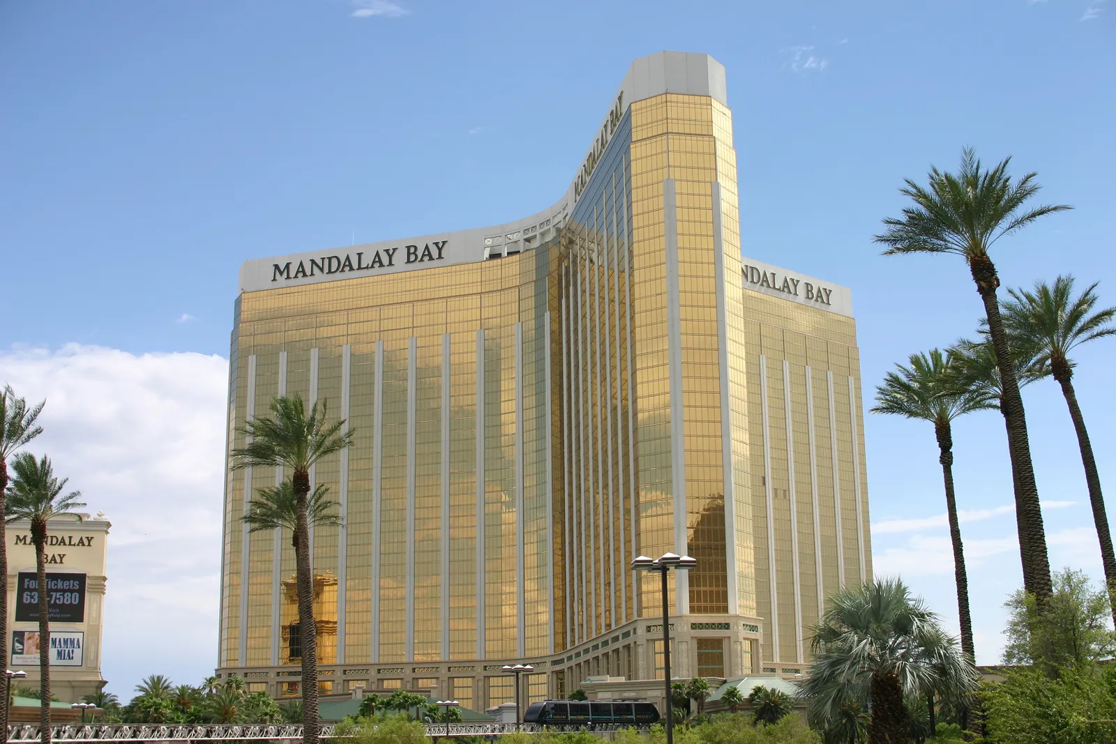 The gold glass towers of Mandalay Bay at the south end of Las Vegas Boulevard, with palm trees along the frontage under a blue sky