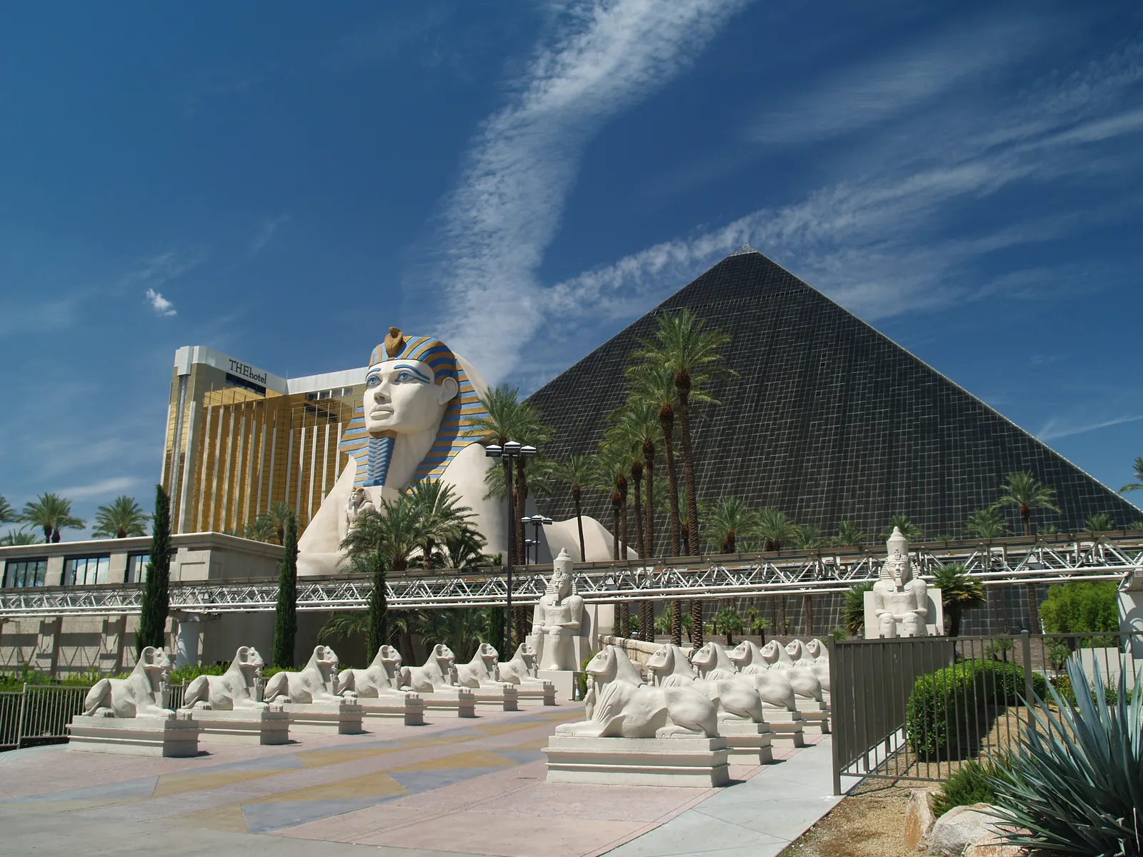 The black glass pyramid of the Luxor in Las Vegas with its giant sphinx and an avenue of smaller sphinx statues leading up to the entrance under a blue sky
