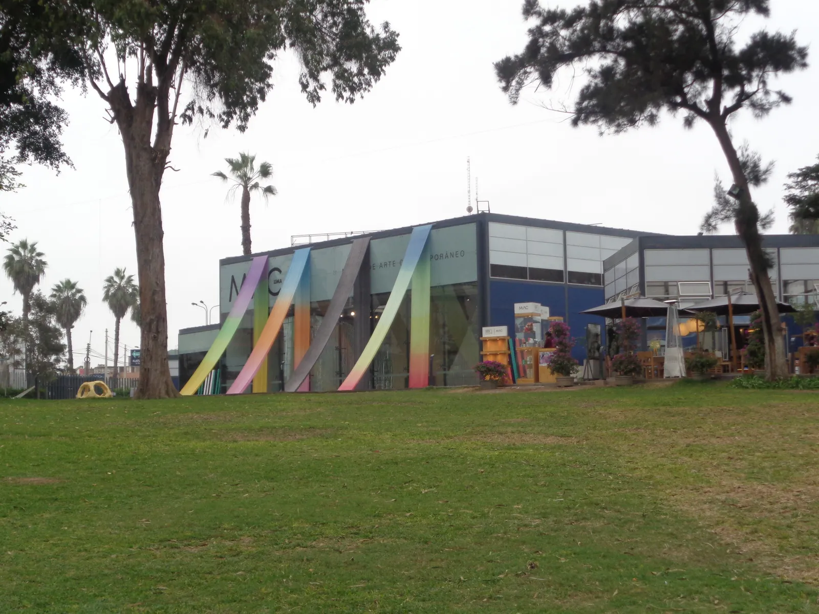 The low glass-fronted MAC Lima building on Avenida Grau in Barranco, seen across a lawn, with coloured vertical stripes painted across its facade