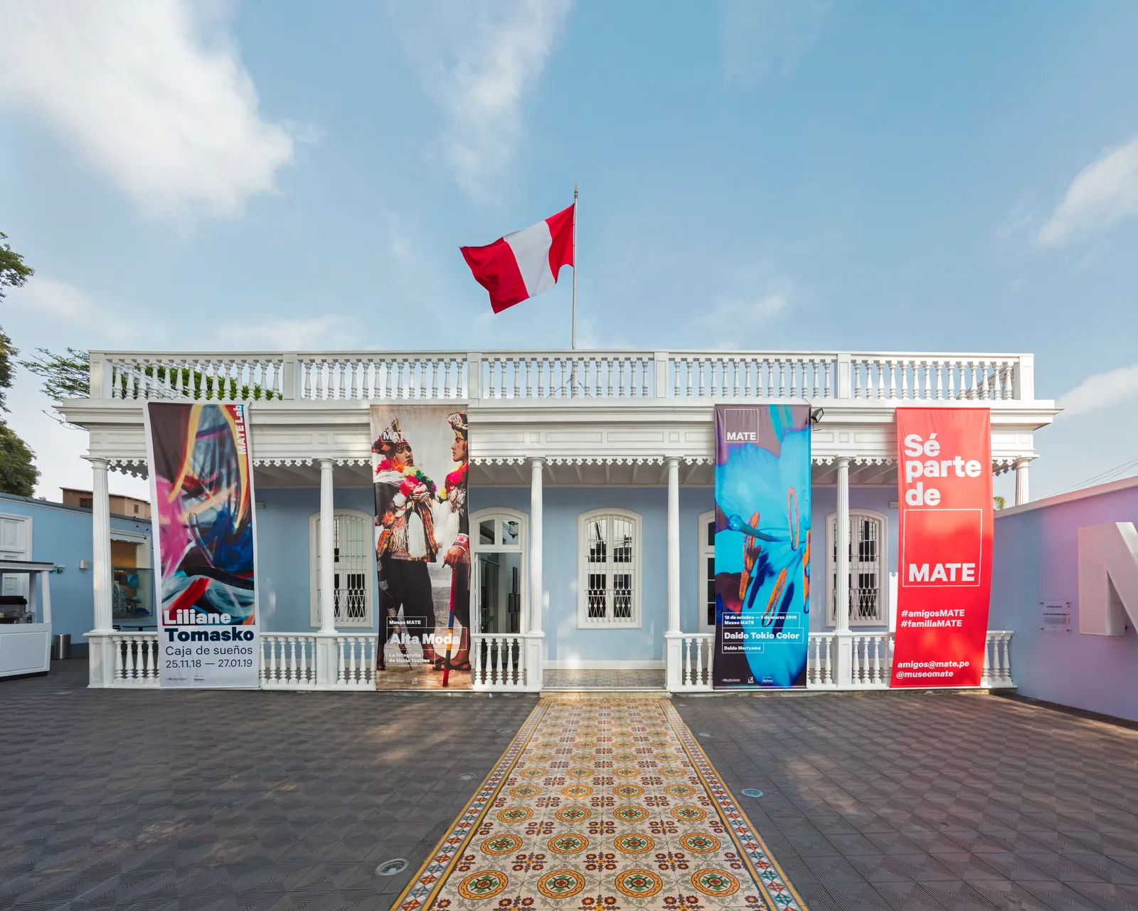 The white balustraded front of the MATE photography museum on Avenida Pedro de Osma in Barranco, Lima, hung with exhibition banners above a patterned tiled walkway