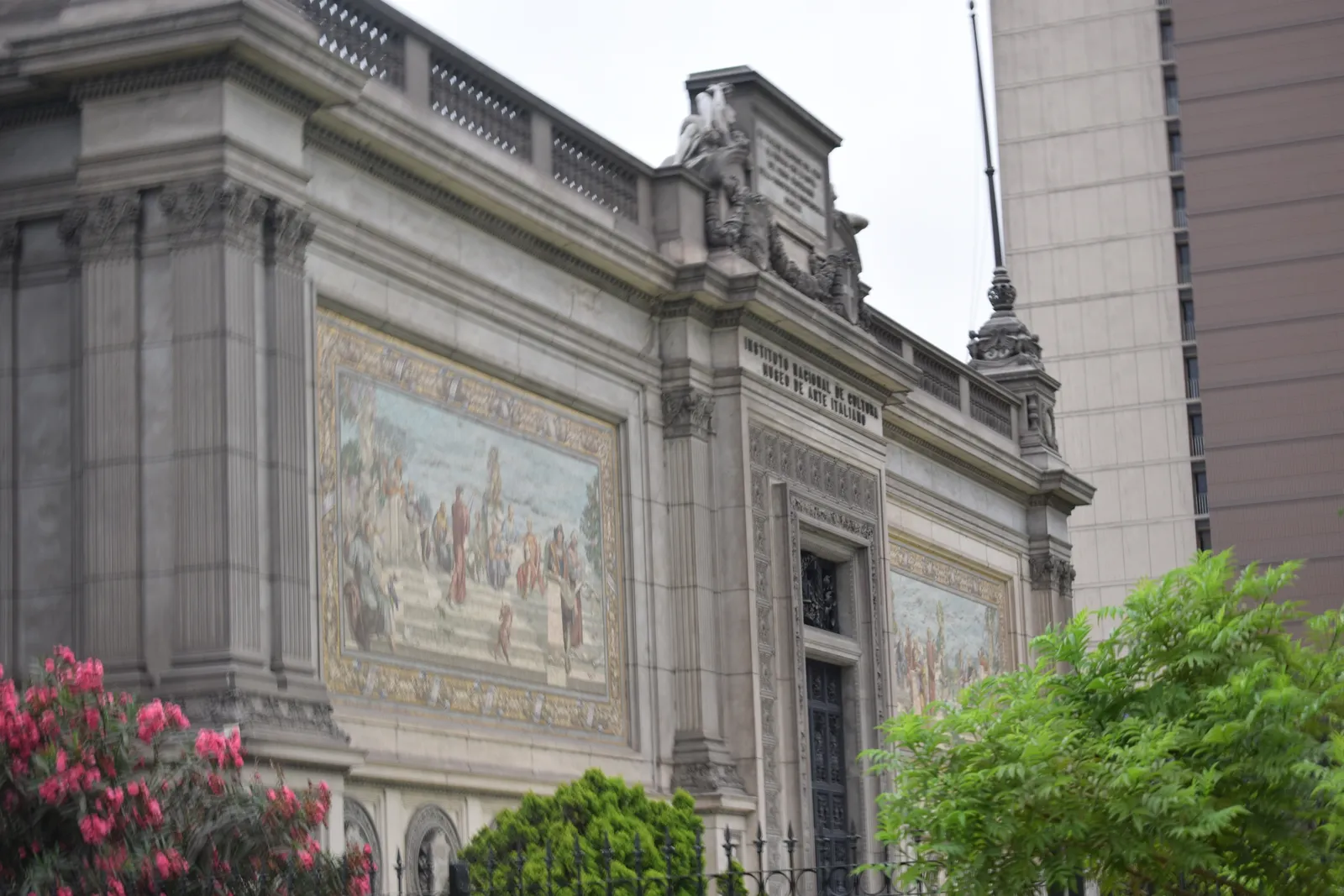 The stone front of the Museum of Italian Art in Lima, with two long tiled mosaic panels set into the wall on either side of the entrance and a figure carved above the parapet
