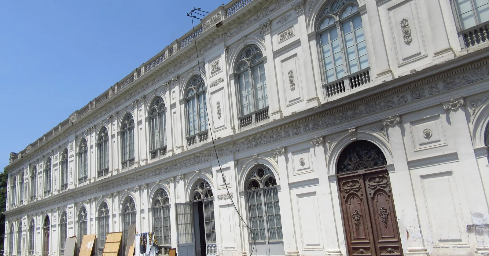 The long white neoclassical front of the Palacio de la Exposición in Lima, two storeys of arched windows and moulded panels running away under a clear sky