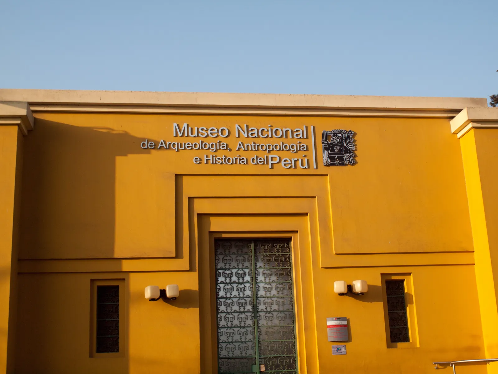 The ochre-yellow front of the National Museum of Archaeology, Anthropology and History of Peru on Plaza Bolívar in Pueblo Libre, Lima, with its name in metal letters above a dark iron door