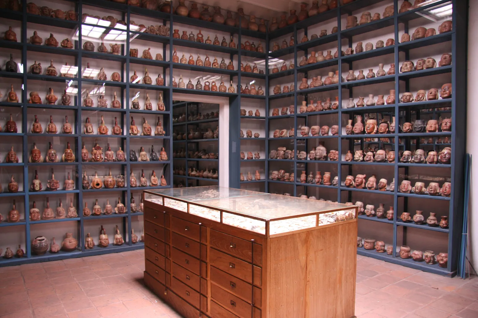 A room in Museo Larco lined floor to ceiling with blue metal shelving holding hundreds of ancient Peruvian pots, with a wooden cabinet in the middle of the floor