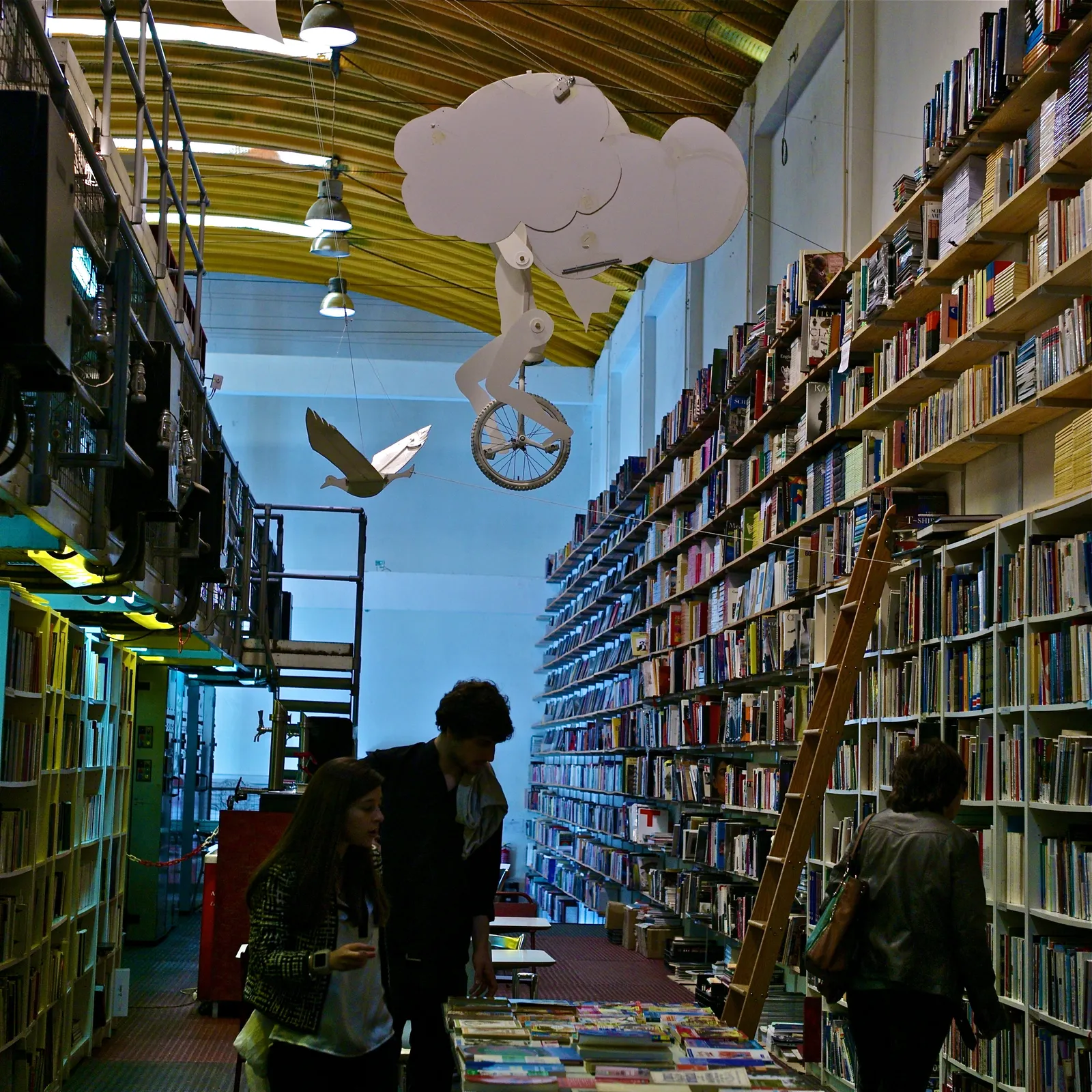 An aisle in the Ler Devagar bookshop in Lisbon, with shelves of books running floor to ceiling on both sides and a rolling ladder against them