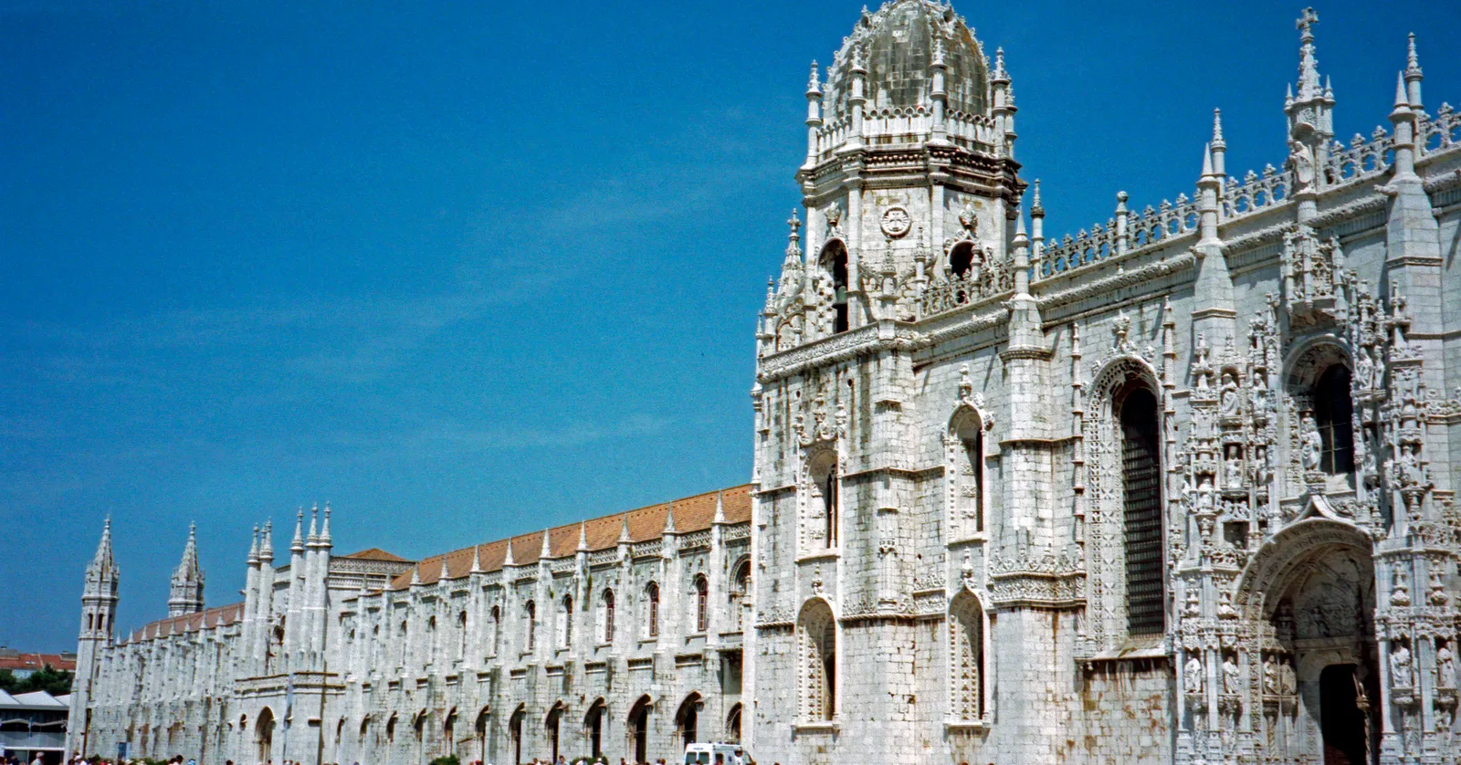The long carved limestone south front of Jerónimos Monastery in Belém, Lisbon, with its arcade of pinnacled bays under a clear blue sky
