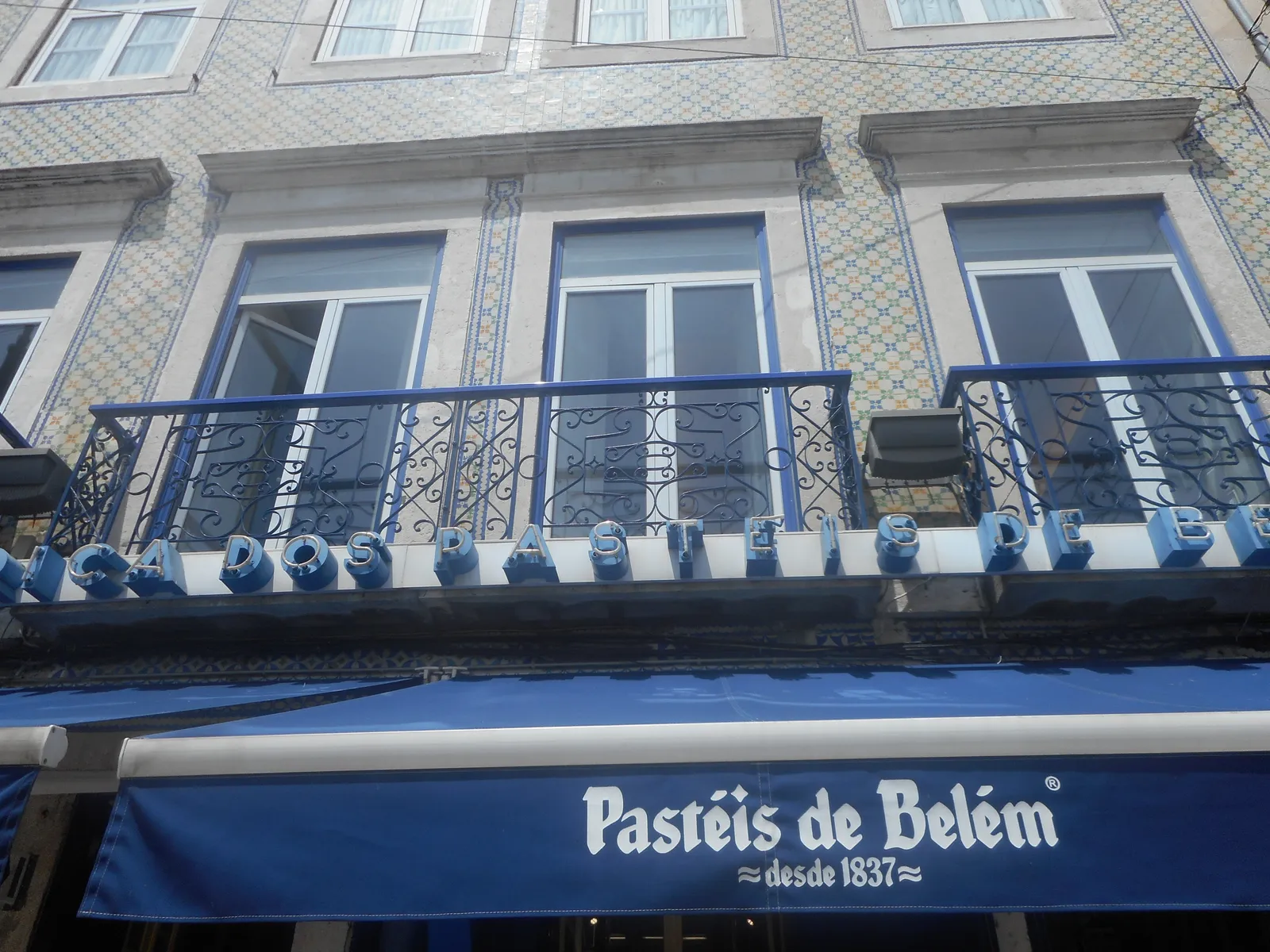 The blue awning and tiled facade of the Pastéis de Belém pastry shop in Lisbon, lettered with the year 1837