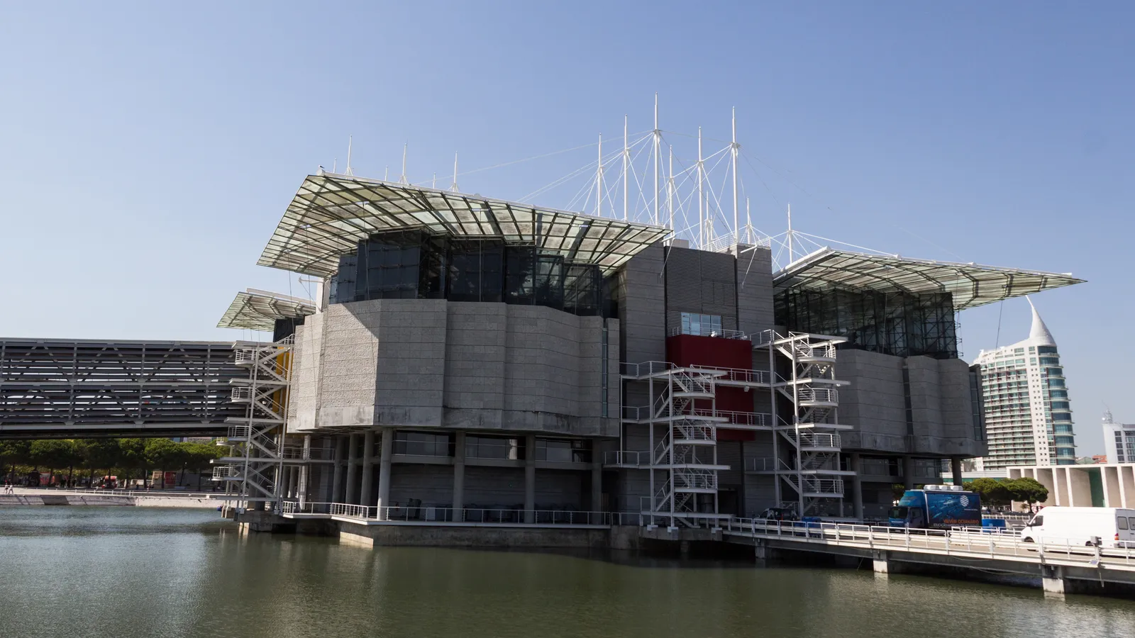 The Lisbon Oceanarium, a grey concrete and glass building standing in its own lagoon at Parque das Nações, with the Vasco da Gama tower behind it