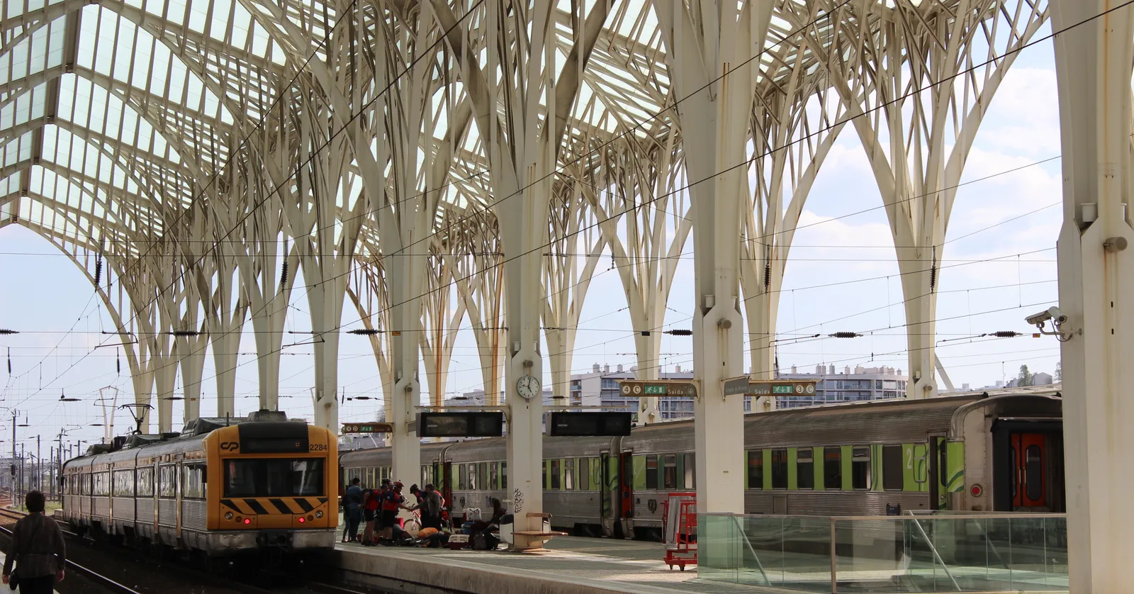 The white branching steel columns and glass canopy over the elevated platforms at Lisbon's Oriente station, with trains waiting alongside