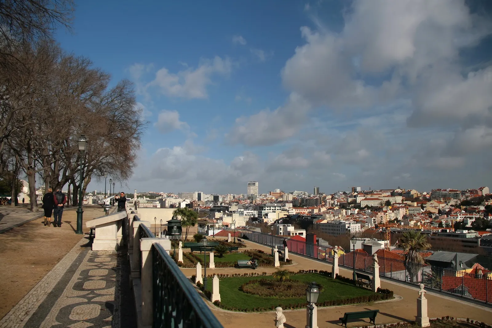 The balustraded terrace at the São Pedro de Alcântara viewpoint in Lisbon, its patterned pavement running above a terraced garden with the city beyond