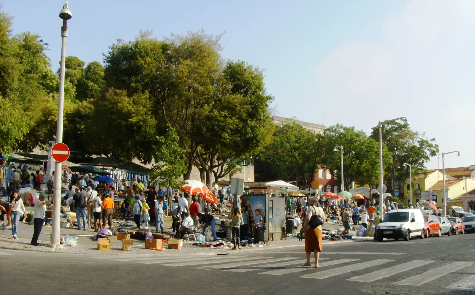 Stalls and shoppers spread out under trees along Campo de Santa Clara in Lisbon during the Feira da Ladra flea market