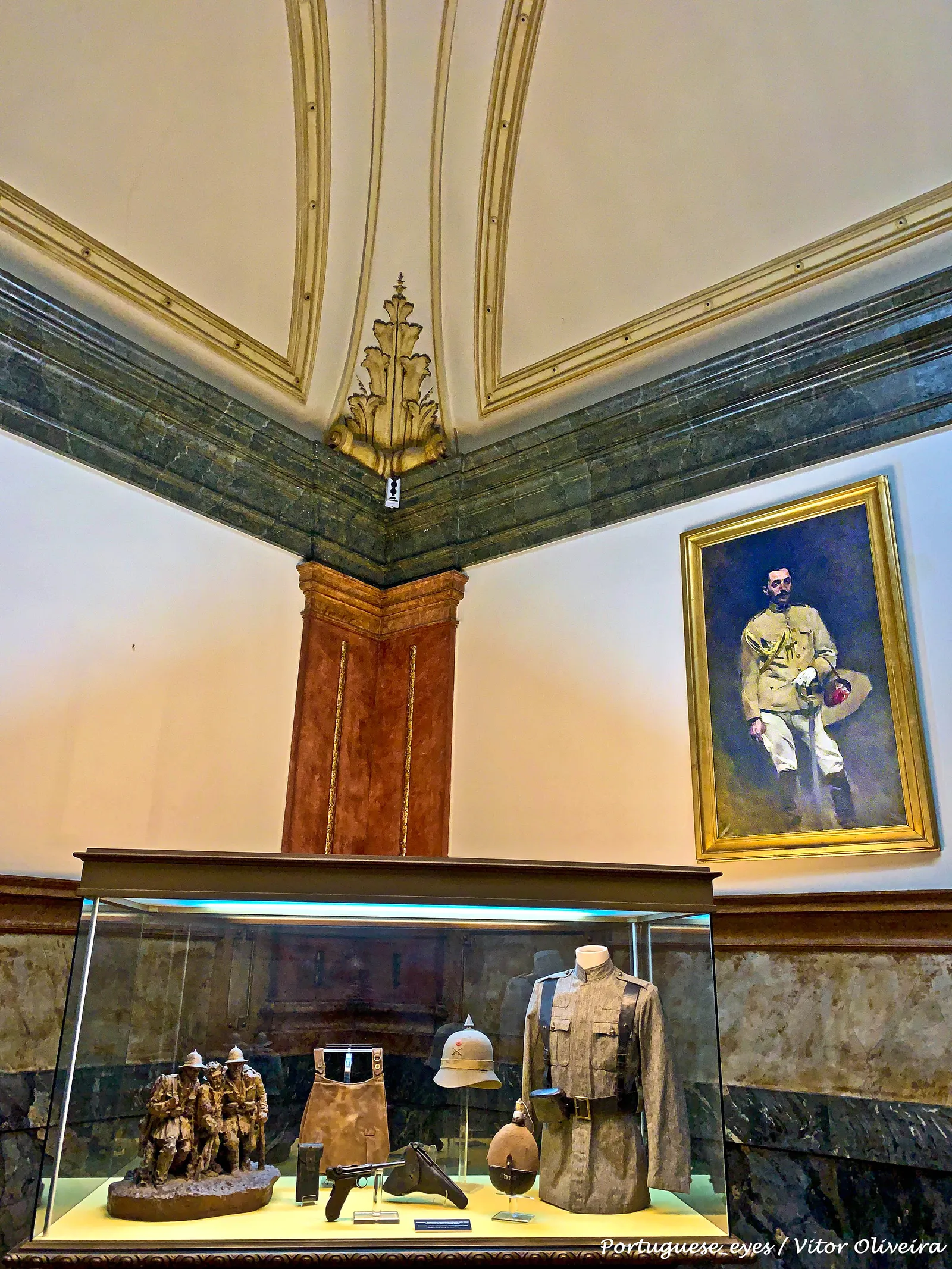A painted and gilded ceiling above a display case of uniforms and helmets inside the Military Museum in Lisbon
