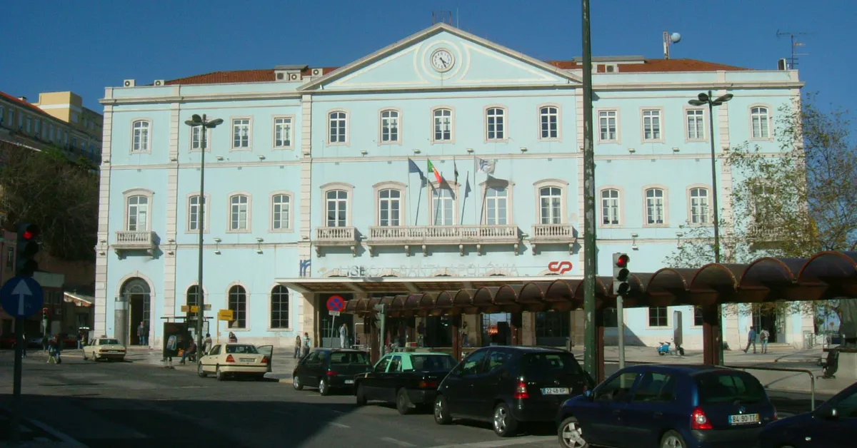 The long white facade of Santa Apolónia railway station in Lisbon, with a clock above the central entrance and a canopy over the doors