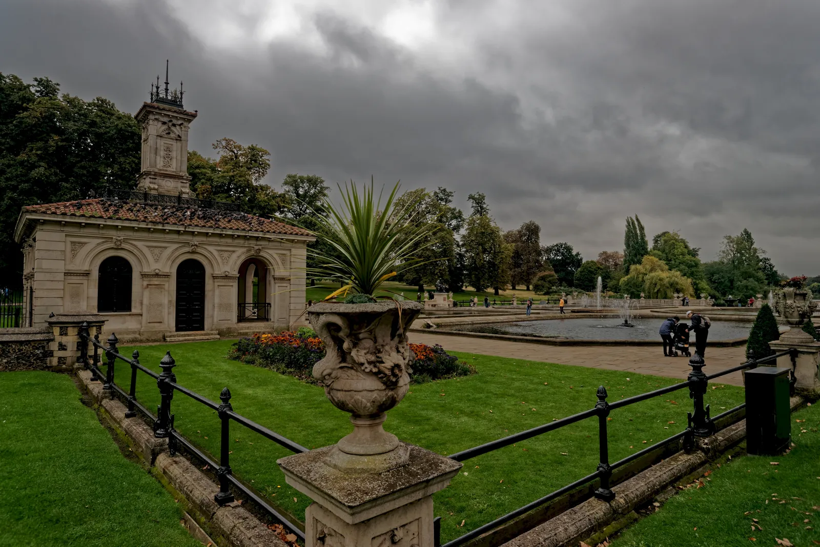 The Italian Gardens in London's Kensington Gardens, with a stone urn, clipped lawns, an ornamental pool and the pavilion's tower