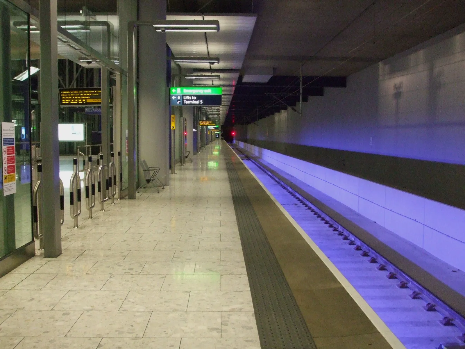 An empty underground platform at Heathrow's Terminal 5 station, with glass screens along the edge and a sign pointing to the lifts up to the terminal