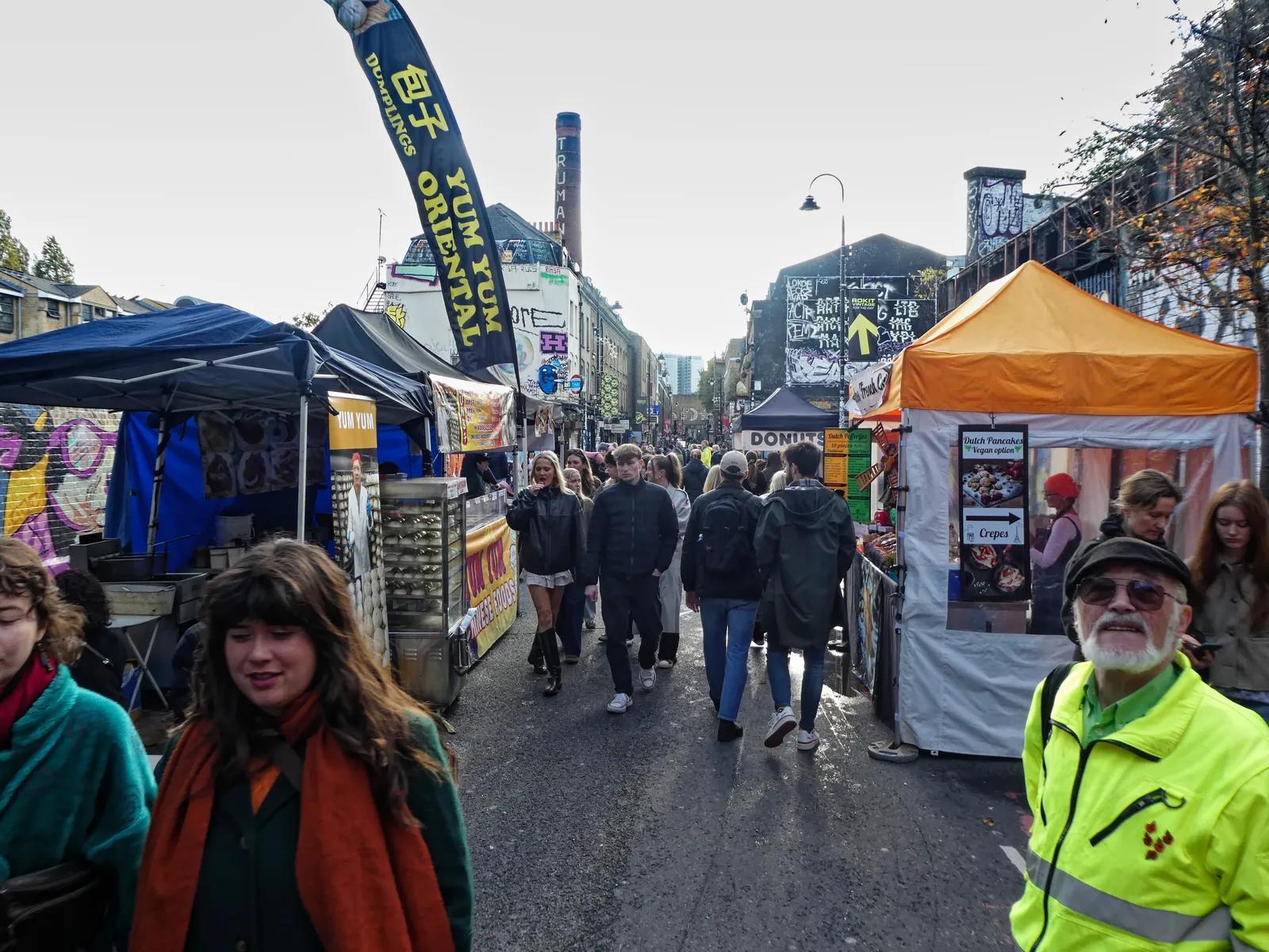 Food stalls and crowds on Brick Lane with the Truman Brewery chimney in the background