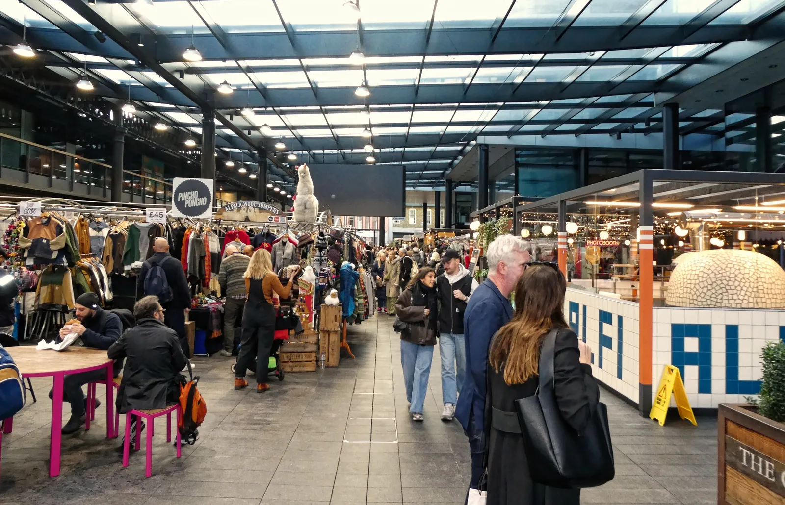 Shoppers browsing clothing and craft stalls under the glass roof of Old Spitalfields Market