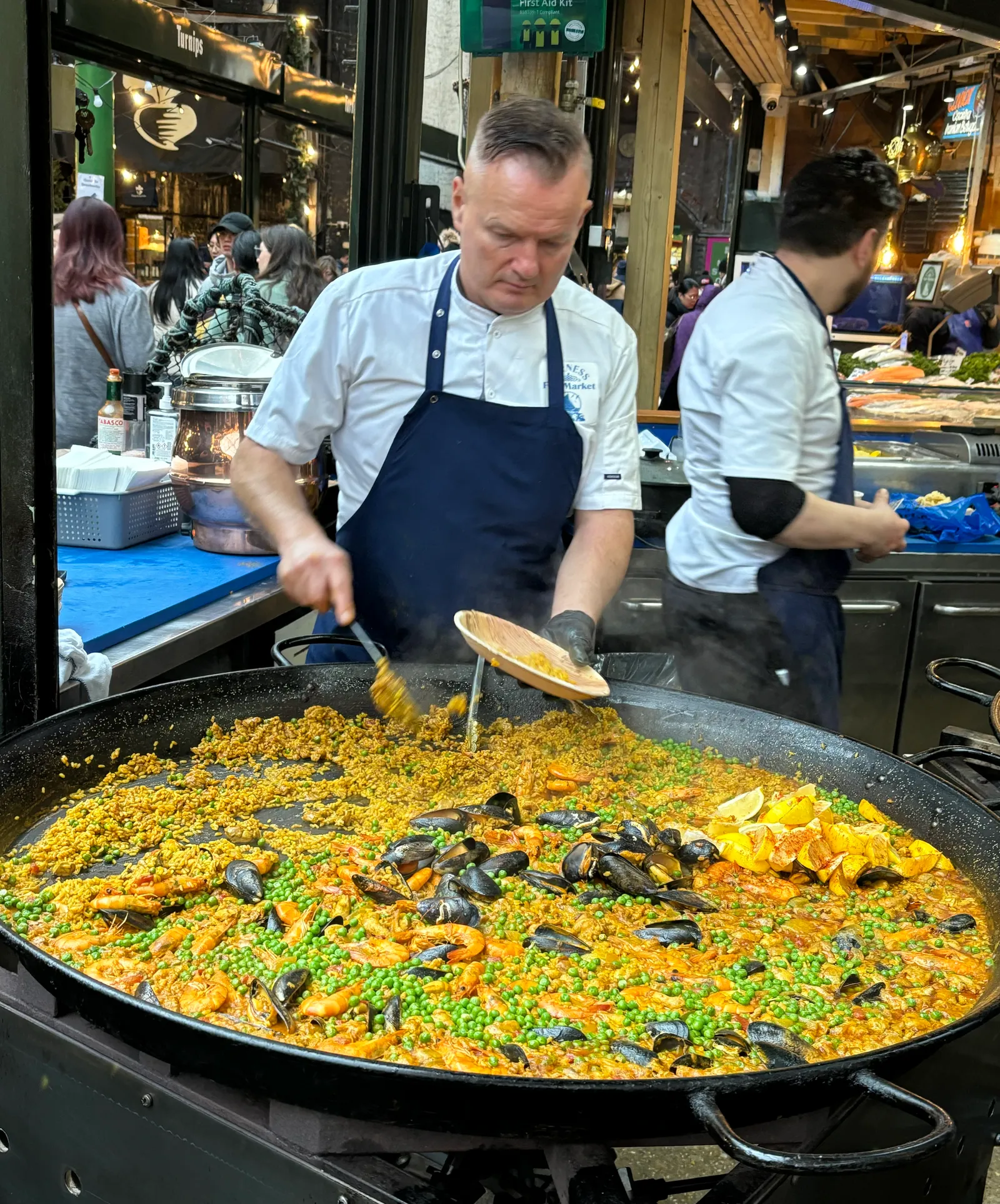 A vendor serving fresh paella from a giant pan at a Borough Market food stall