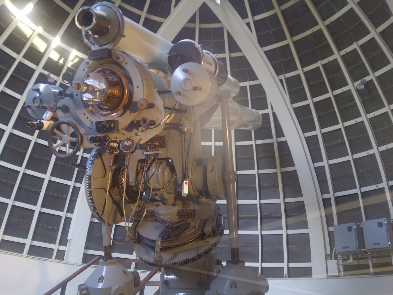 The Zeiss refracting telescope inside its dome at Griffith Observatory, a long pale metal tube on a heavy geared mount, with the ribbed white interior of the dome curving overhead