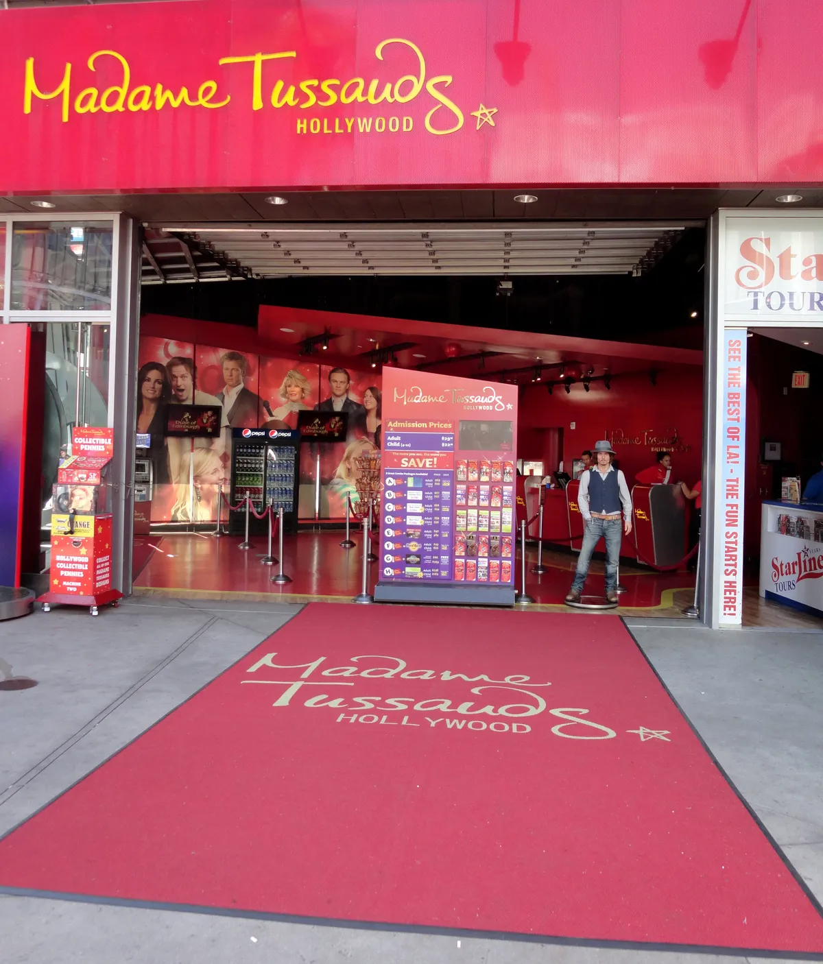 The entrance to Madame Tussauds Hollywood, a red frontage with the name in script above an open doorway and a red carpet running out across the pavement towards the street
