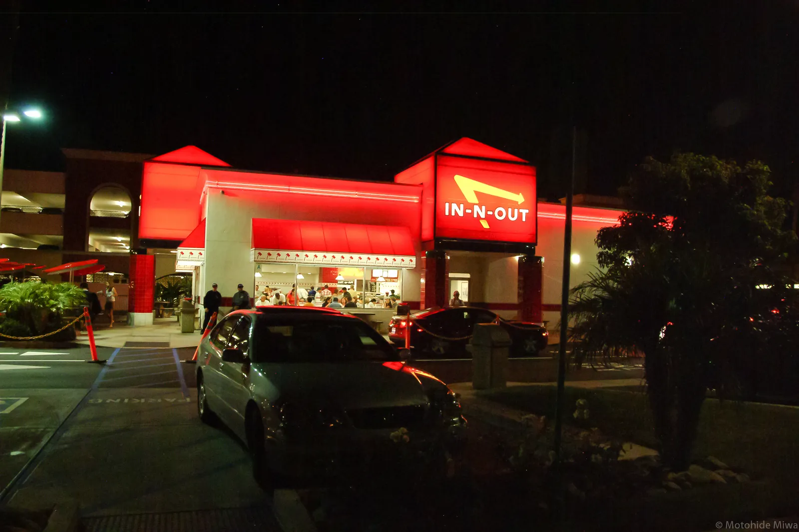 An In-N-Out Burger on Sepulveda Boulevard near Los Angeles airport at night, the red and white building lit up under a broad canopy with cars queuing in the forecourt and palms behind