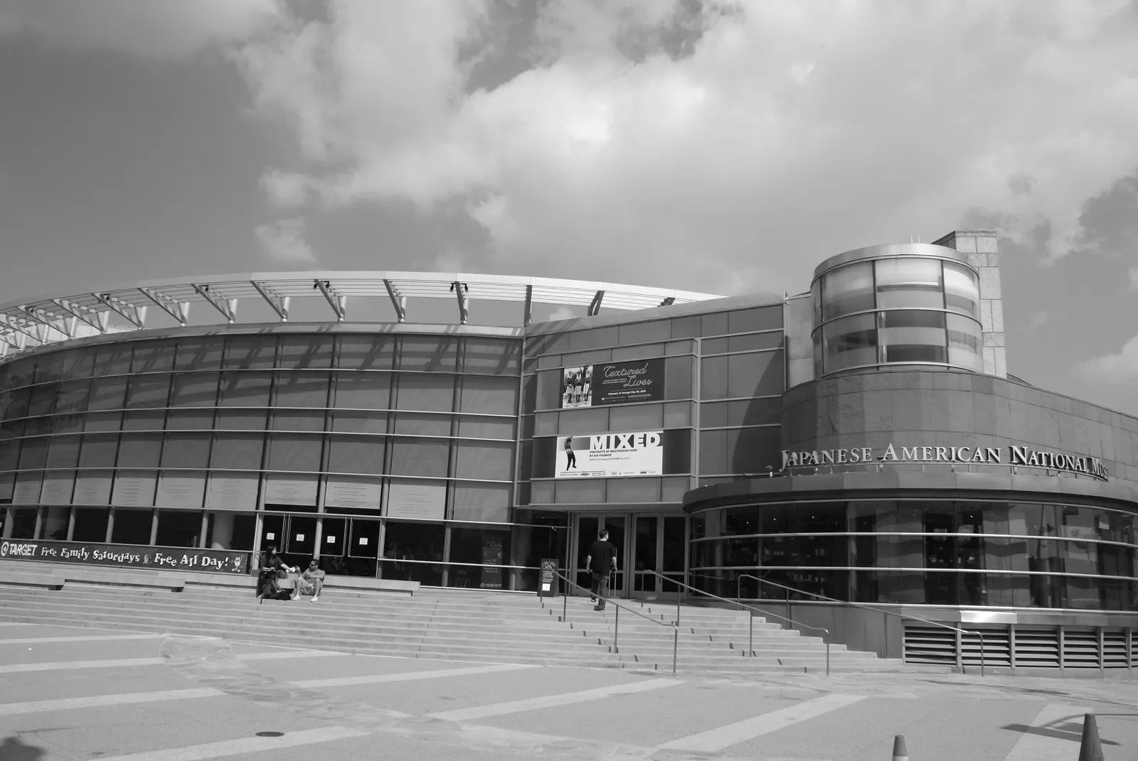 The Japanese American National Museum pavilion in Los Angeles, a curved glass and stone building with the museum's name lettered across the front, above a broad flight of steps