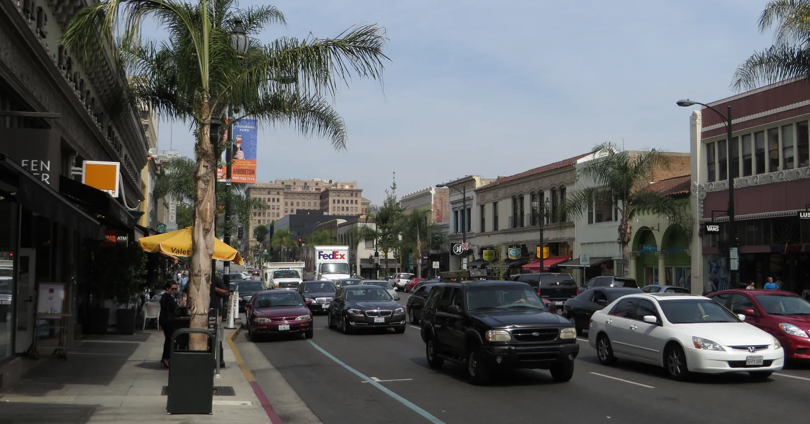 Colorado Boulevard in Old Pasadena, a wide street of two- and three-storey brick and stucco shopfronts with awnings, tall palms along the pavement and traffic moving between them