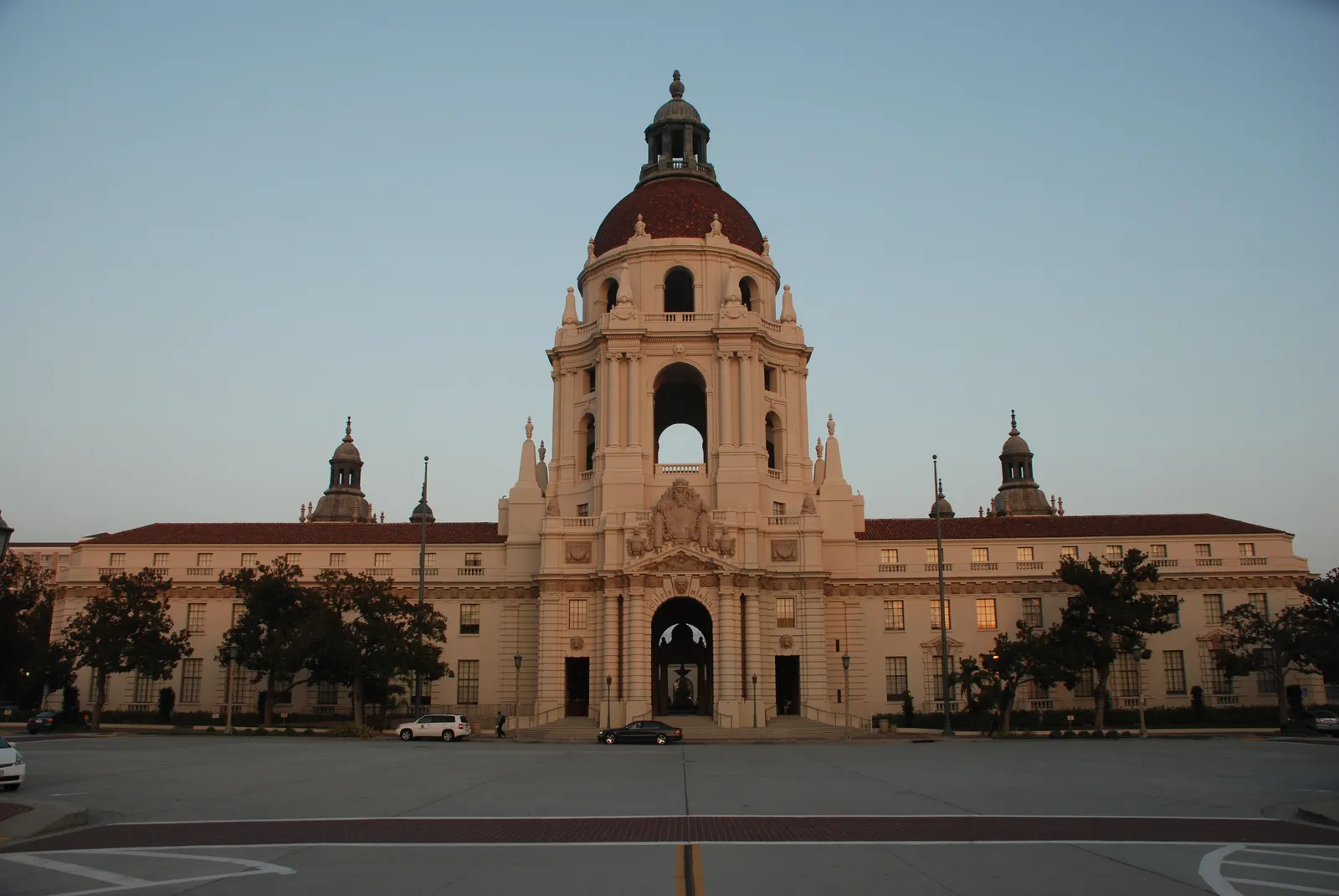 Pasadena City Hall at dusk, a long pale Beaux-Arts building with a red tiled roof and an arched entrance beneath a tall tower topped by a domed cupola