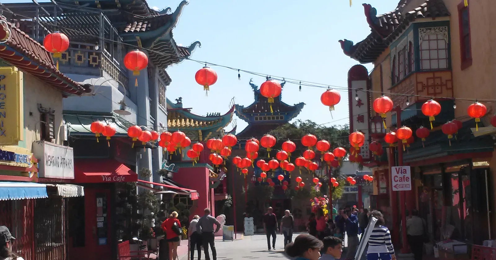 Central Plaza in Los Angeles Chinatown, a pedestrian lane hung with rows of red paper lanterns on wires, pagoda-roofed shopfronts down both sides and people walking the middle of it under a clear sky