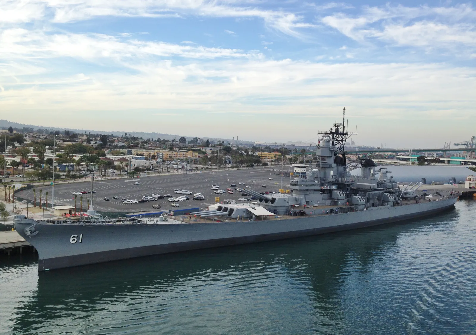 The grey battleship USS Iowa moored on the San Pedro waterfront in Los Angeles, hull number 61 on her bow, with her gun turrets and tower rising amidships