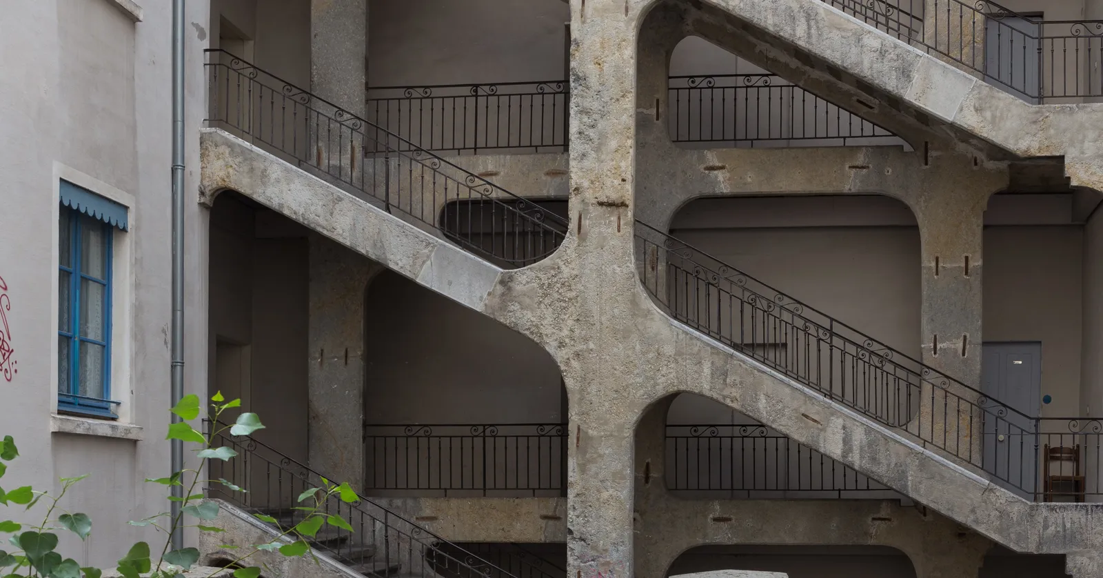 The open staircase inside the Cour des Voraces in Lyon, bare concrete flights zigzagging across the face of a courtyard building over several storeys behind plain iron railings