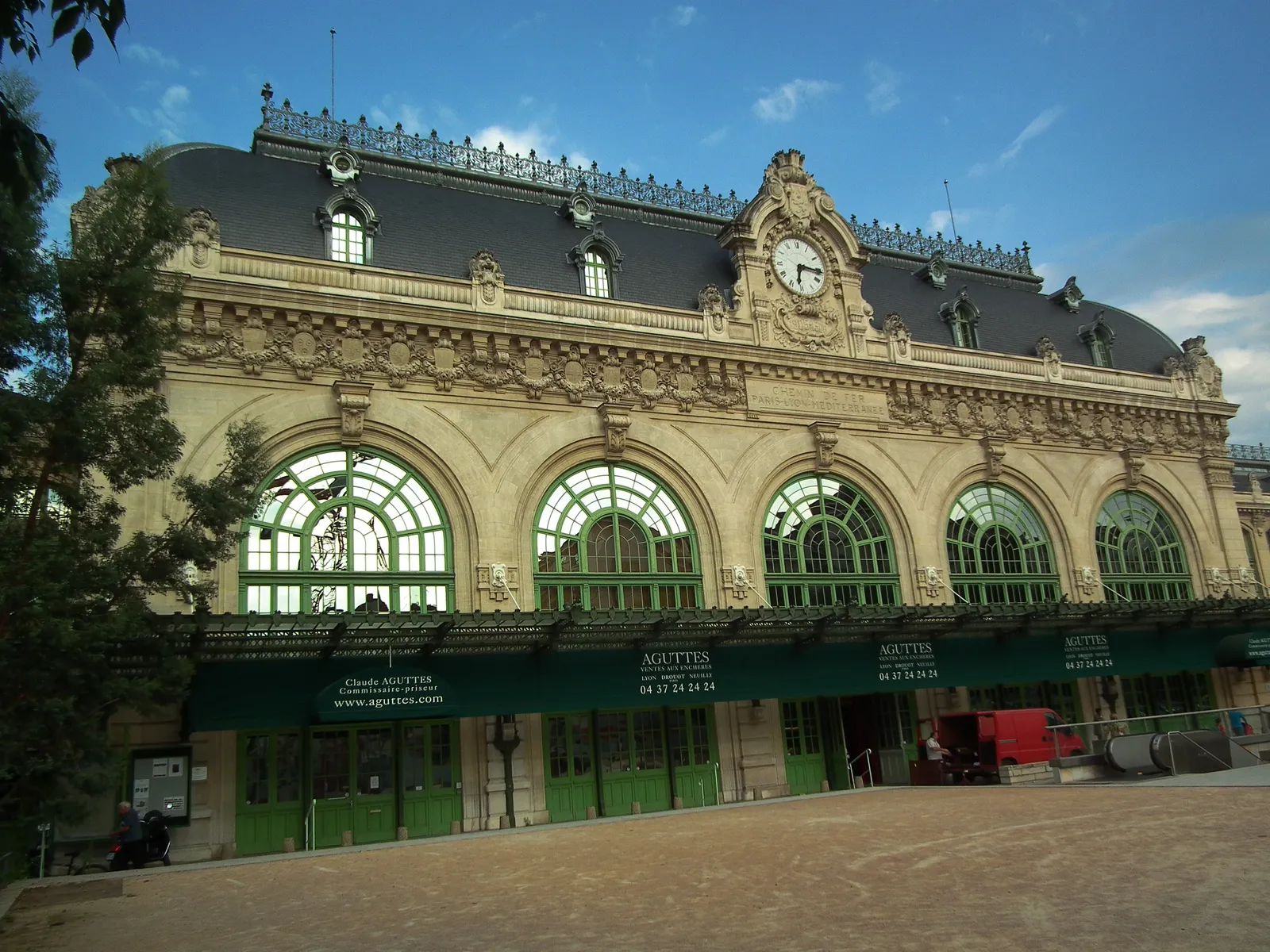 The stone facade of the former Brotteaux station in Lyon, five tall arched windows with ornate carving above them, a clock in the centre gable and a slate roof