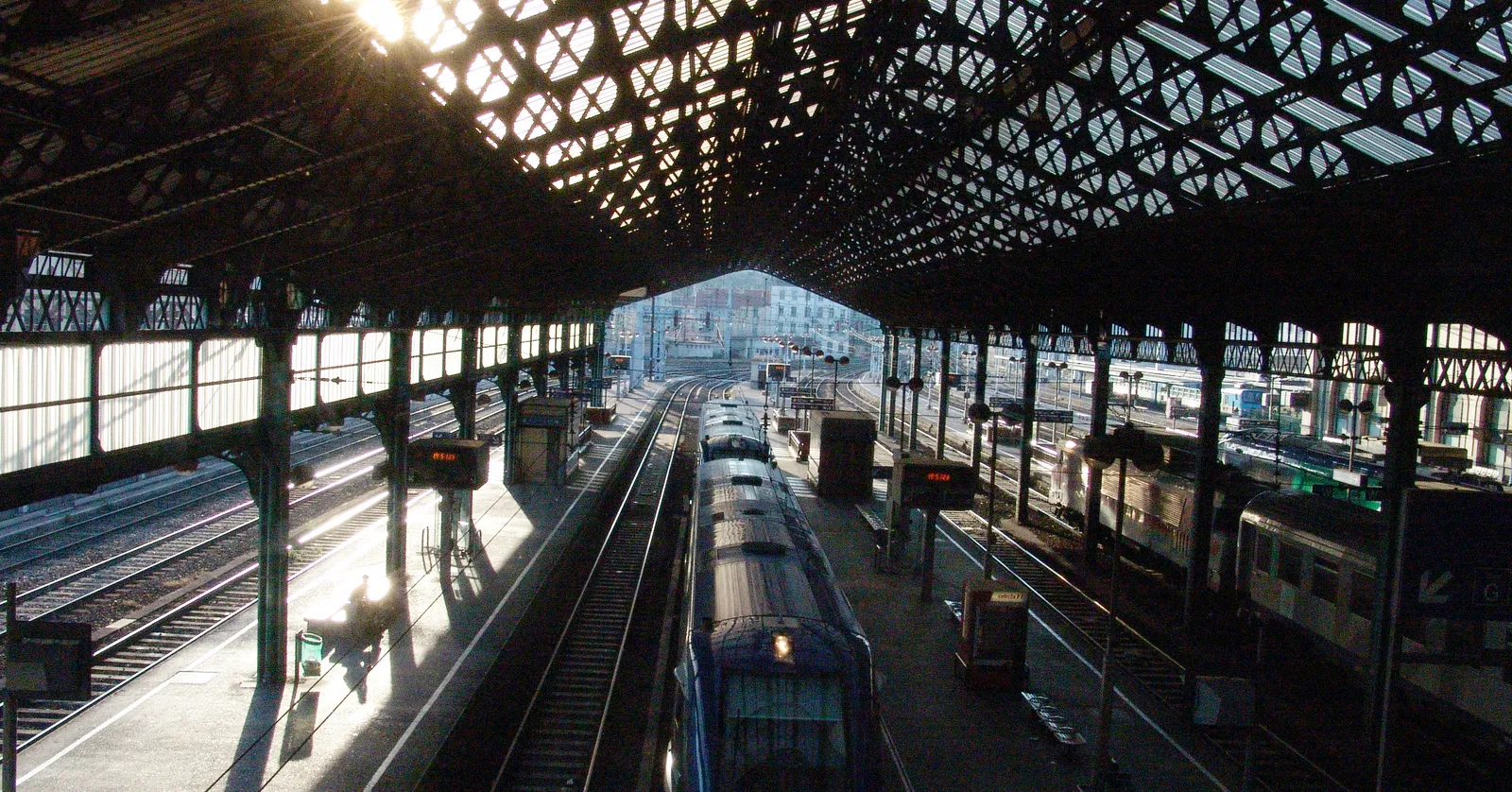 The iron and glass trainshed of Lyon Perrache station seen from above the tracks, sunlight coming through the roof onto trains standing at the platforms below